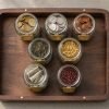 Top-down editorial flat-lay of seven mason jars on a walnut tray, each containing different asset-class objects representing portfolio diversification